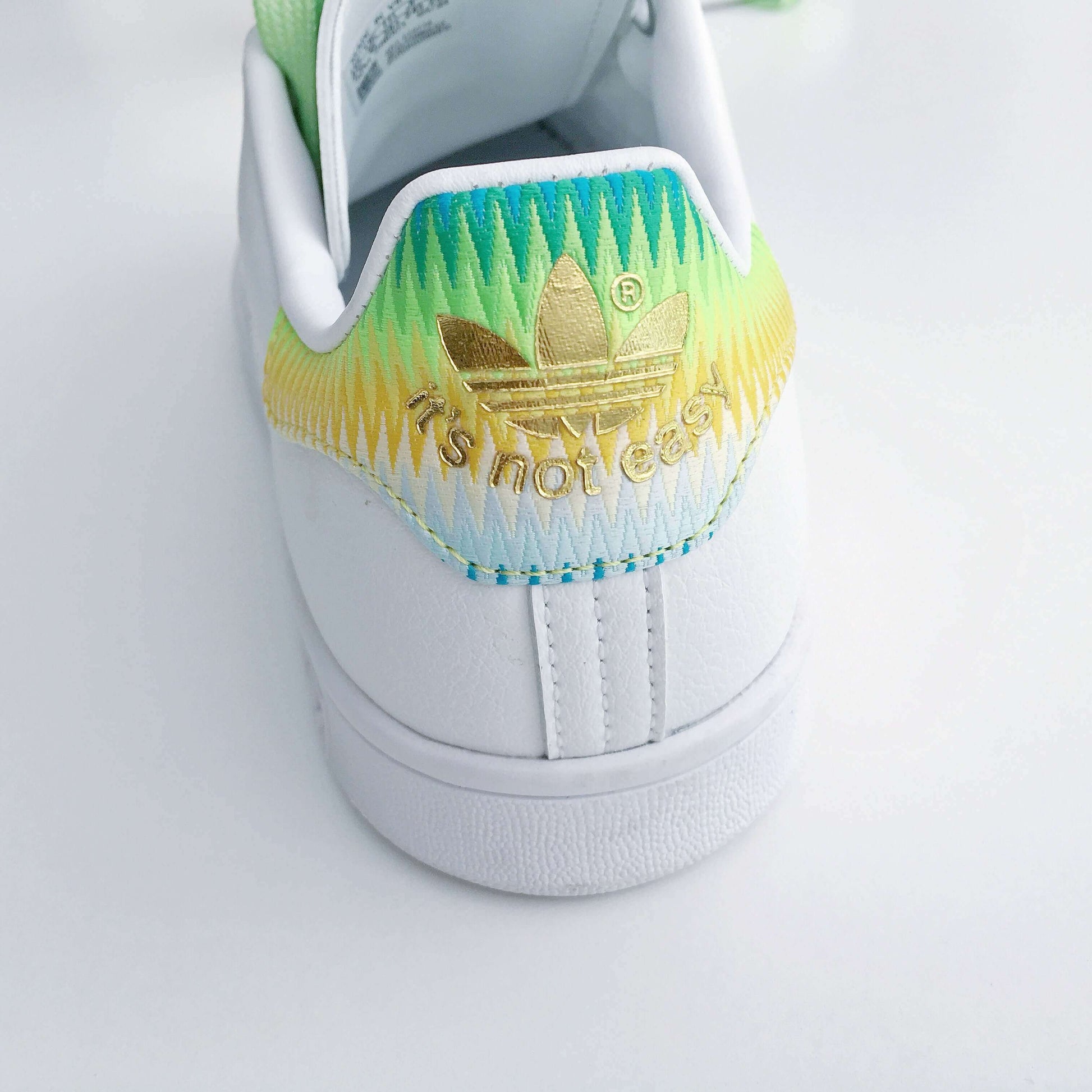 Back view of shoe showing rainbow blue, yellow and green at the top, faded down to white, with gold printed adidas logo.