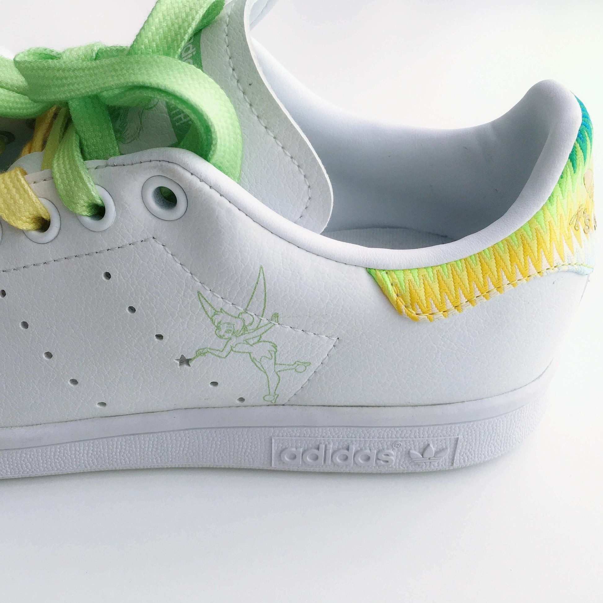 detail view of white adidas stan smith with tinkerbell motif on left outside panel of shoe with star perforation.