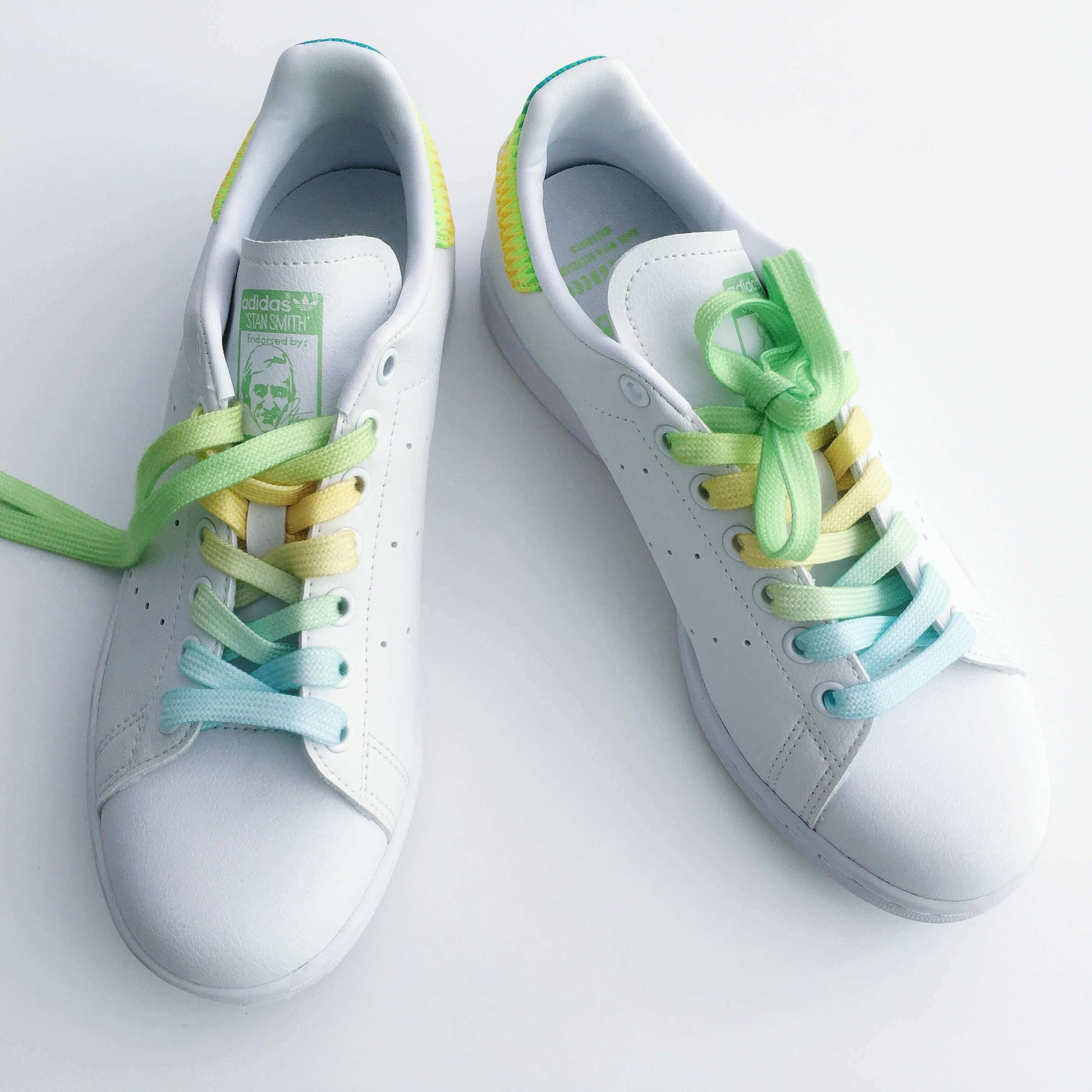 Top view of white shoes, with pale yellow, green and blue laces.