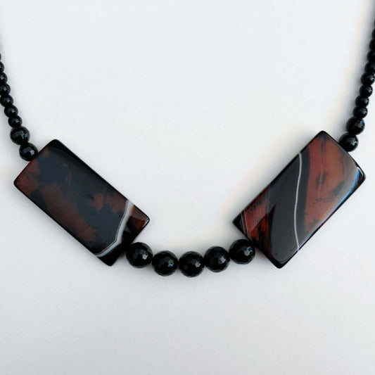 Detail view of the two rectangular agate pieces, set on either side of center front, faceted Obsidian beads between them.