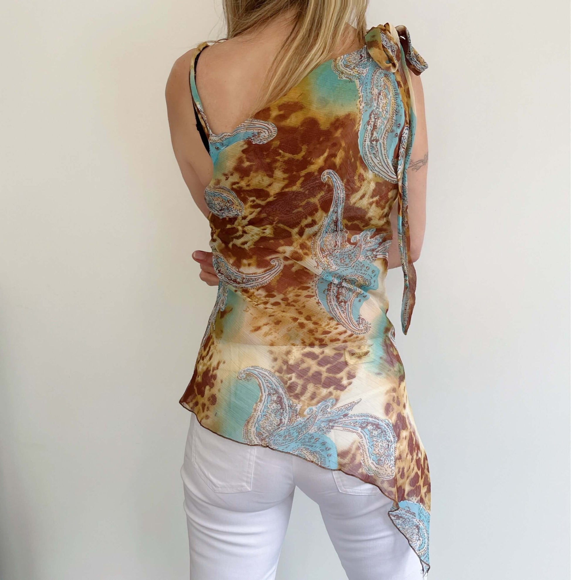 Back view of asymmetrical off shoulder top, which rises from beneath left arm up over right shoulder with a tie.