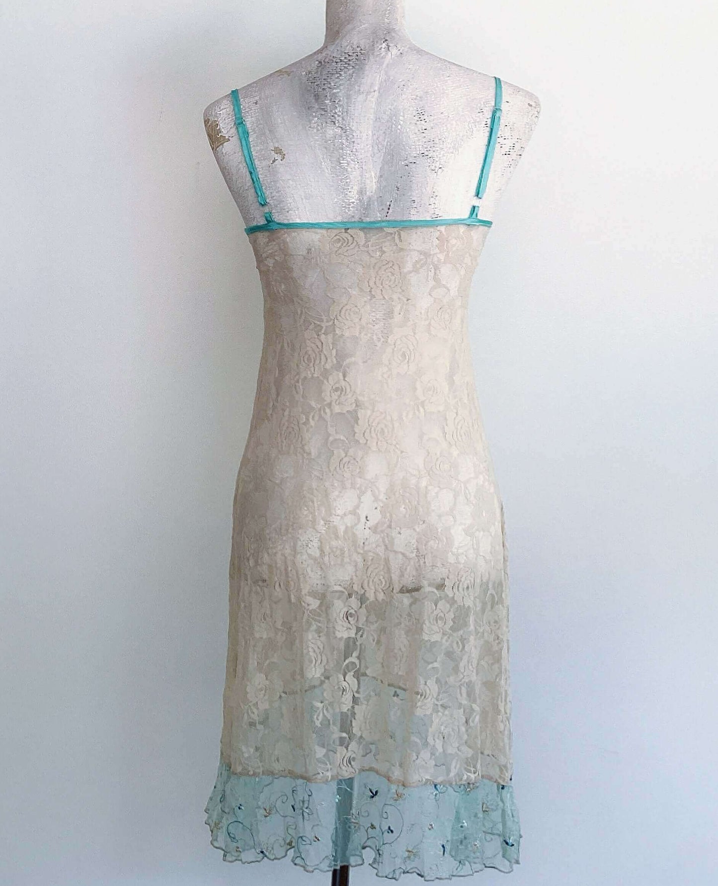 Back view of beige stretch lace floral cami, net embroidered hem frill, with satin aqua adjustable straps.