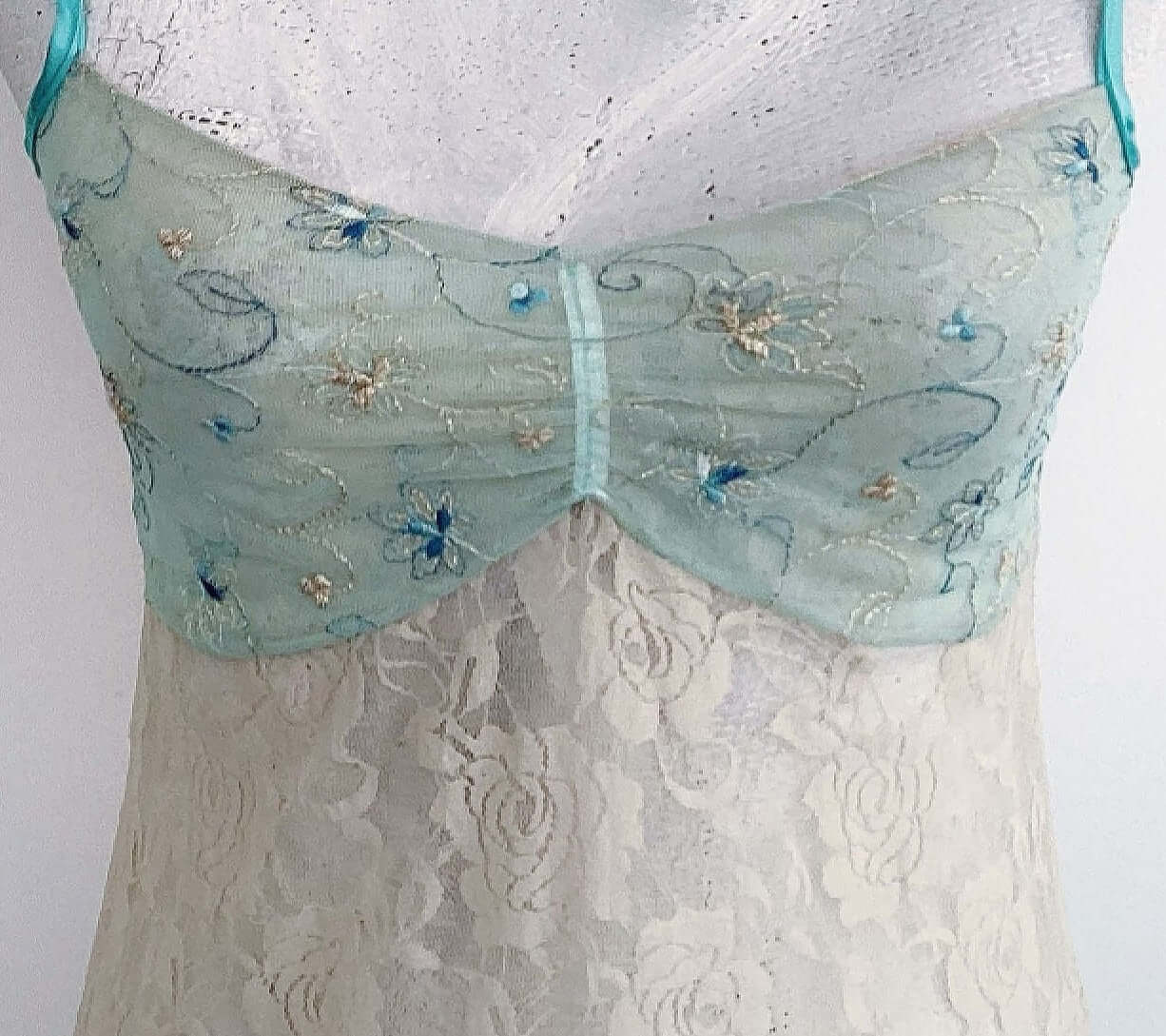 Detail view of beige stretch lace floral cami, with net embroidered aqua bust.