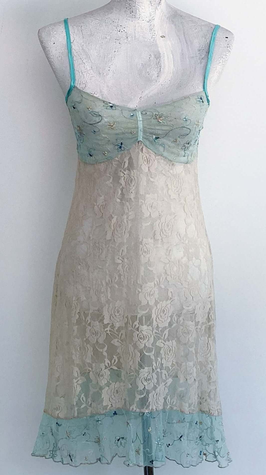 Front view of beige stretch lace floral cami, net embroidered aqua bust and hem frill, with satin aqua adjustable straps.