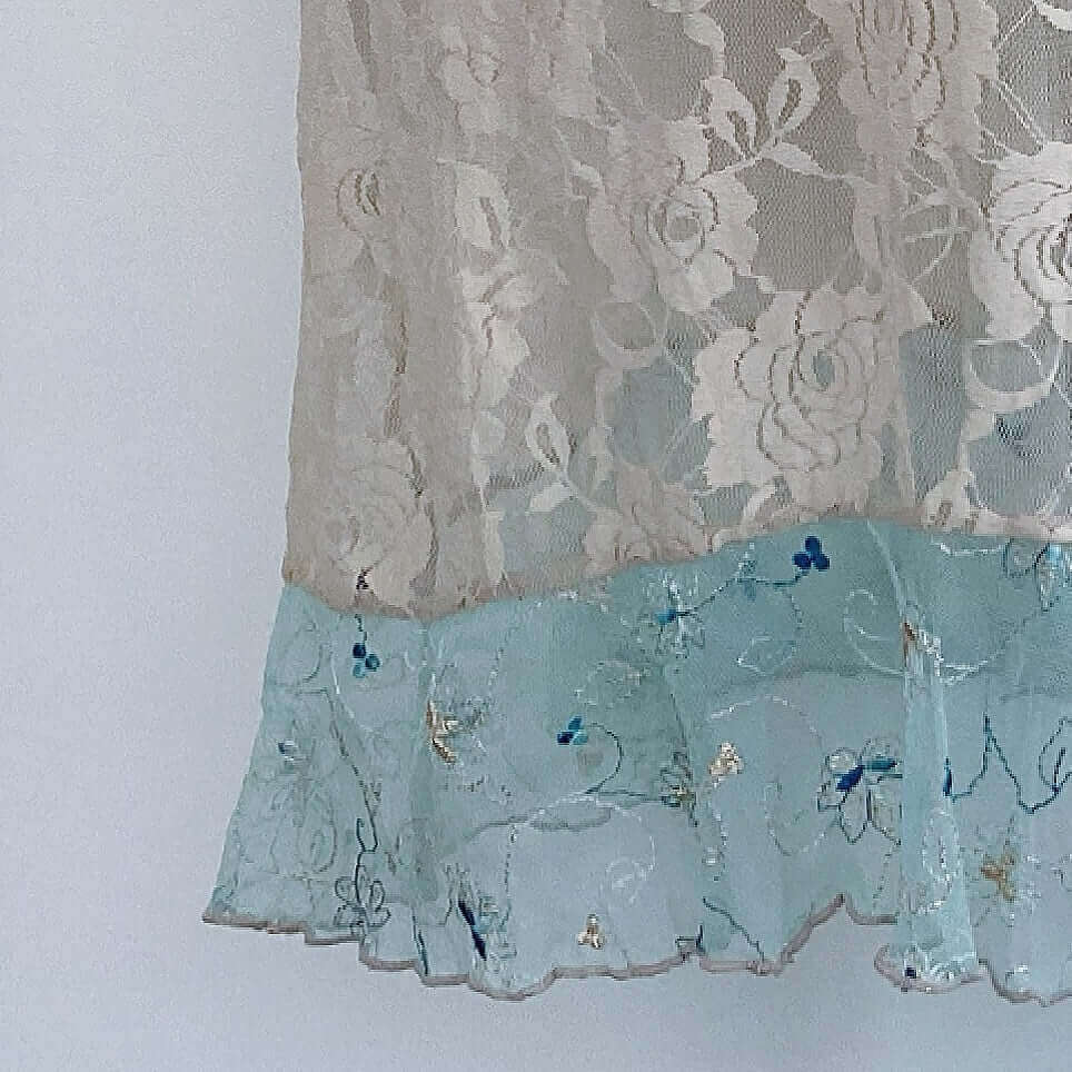 Detail view of beige stretch lace floral fabric, with net embroidered aqua hem frill.