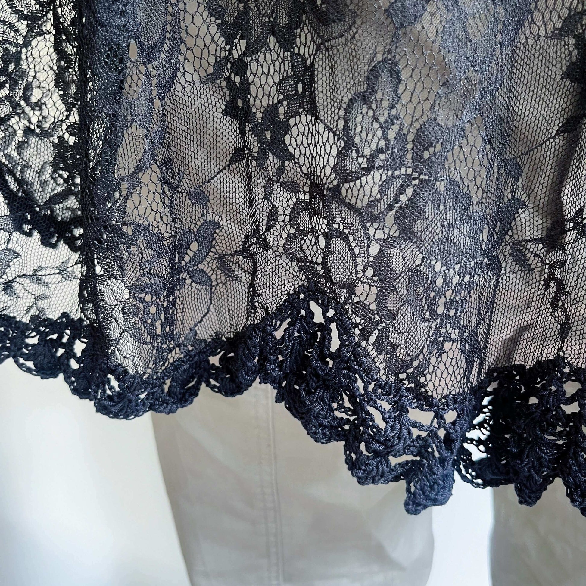 Detail view of black lace swing top, wide scalloped hem, with a band of black crochet.