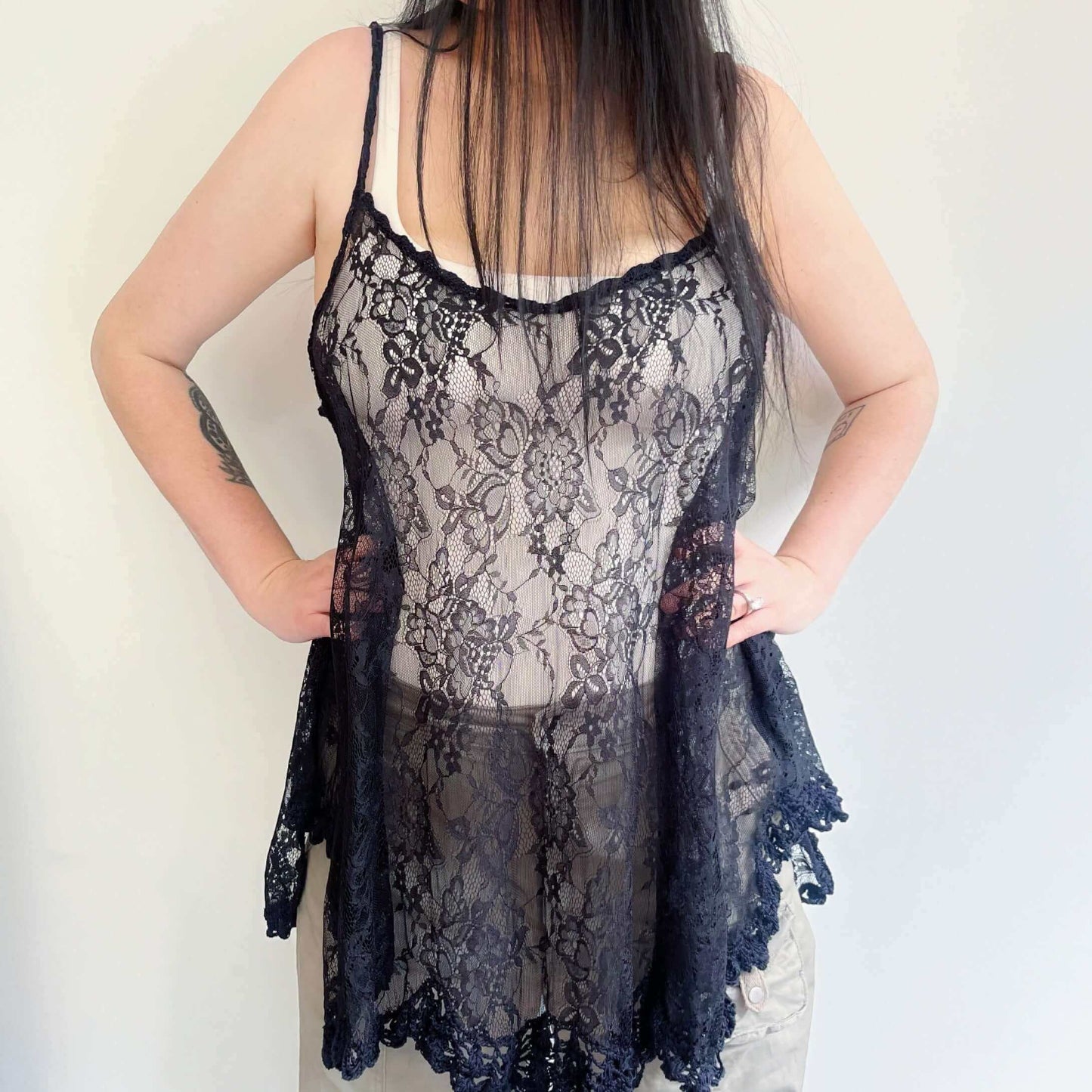 Front view black lace swing top, wide scalloped hem, with a band of black crochet on the hem and straps. Hands on hips.