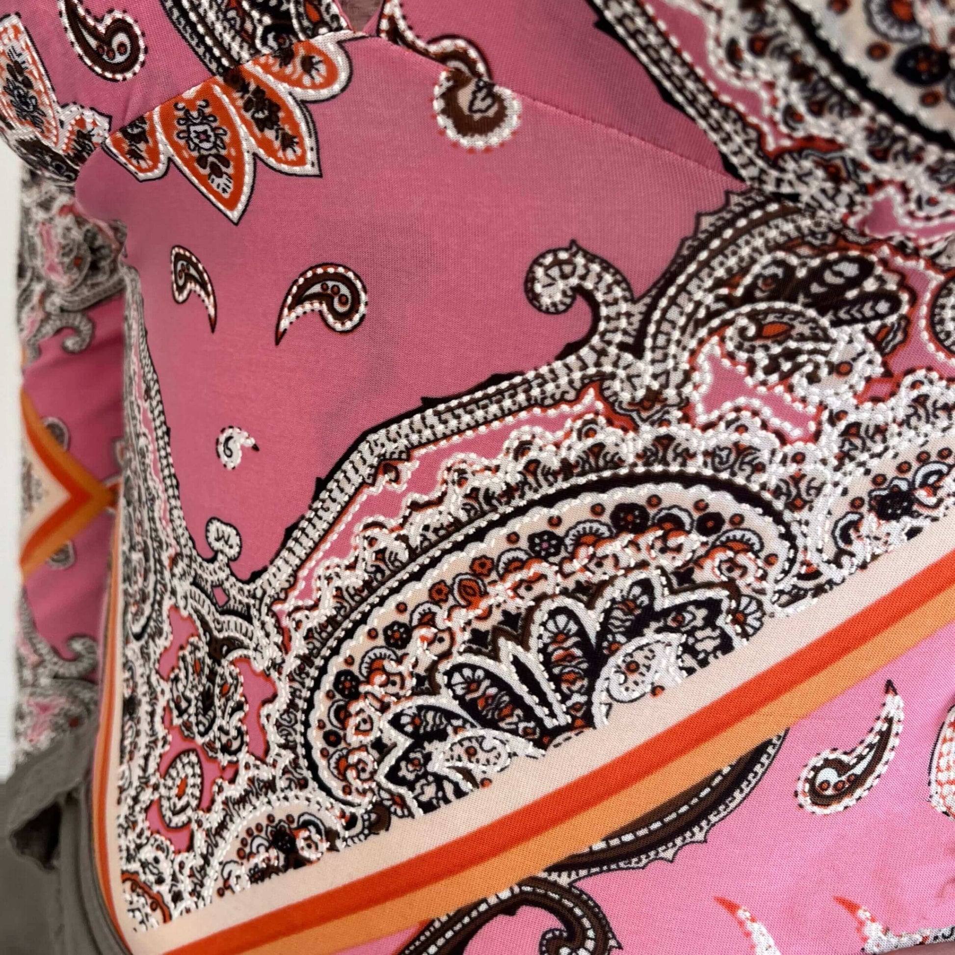 Detailed view of lycra top, showing the floral and geometric print, in pink, orange, brown and white.