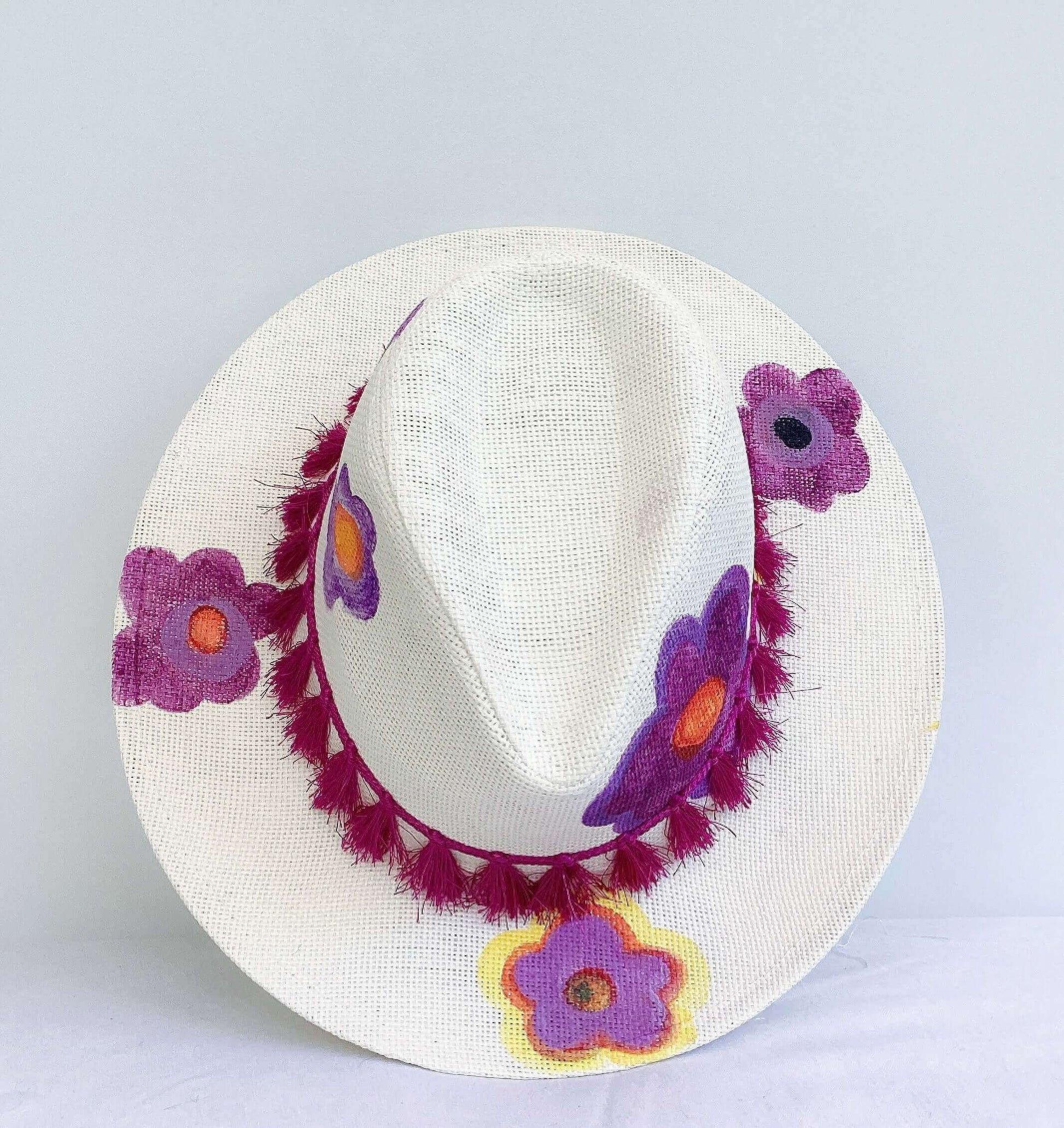 Aerial view of panama hat, black band and magenta fringe at base, painted purple and orange flowers asymmetrically spaced.