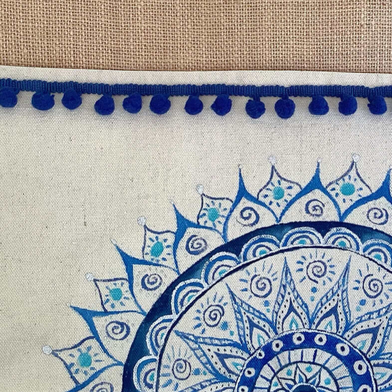 Closeup of bag, with band of hessian at the top, pompoms stitched across in blue, with painted half mandala on lower part.