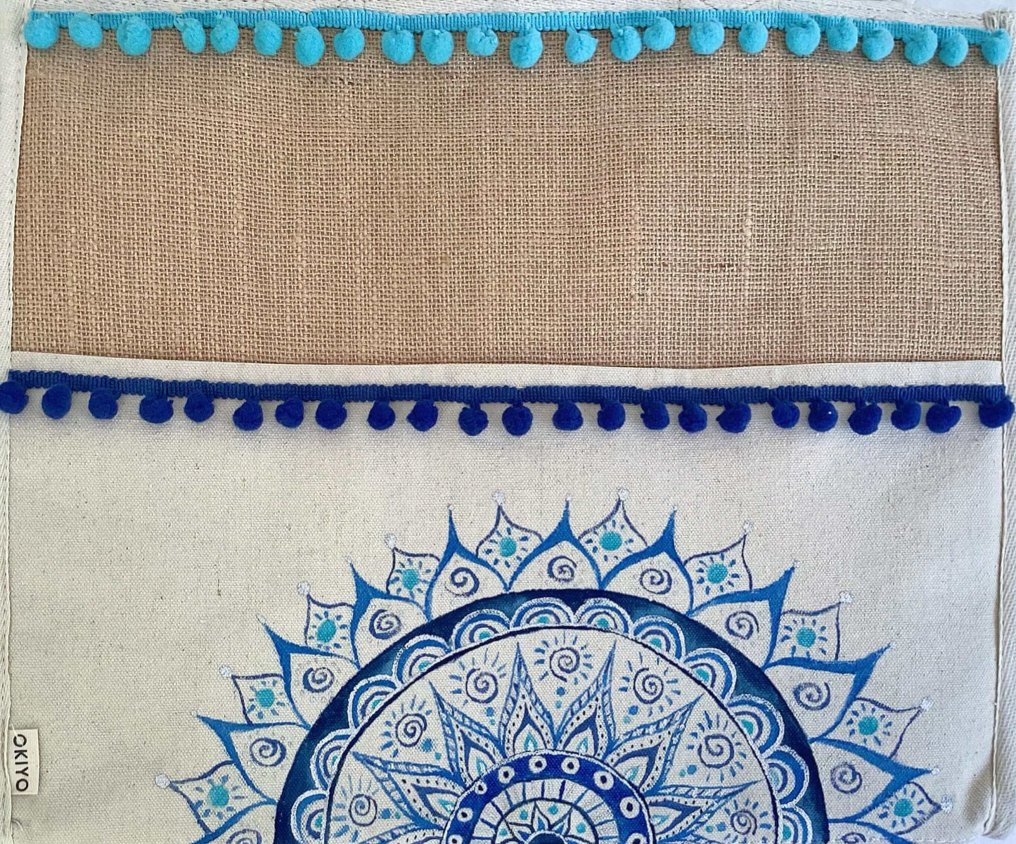 Detail of bag with band of hessian at the top, pompoms stitched across in blue, with painted half mandala on lower part.