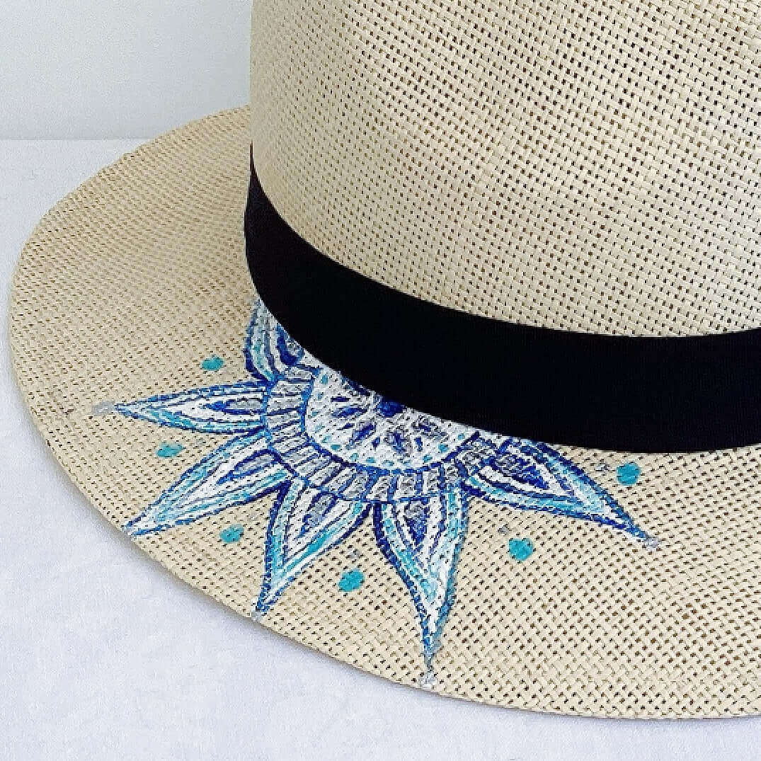 Close up view of panama hat, black band at base, with hand painted blue mandala.