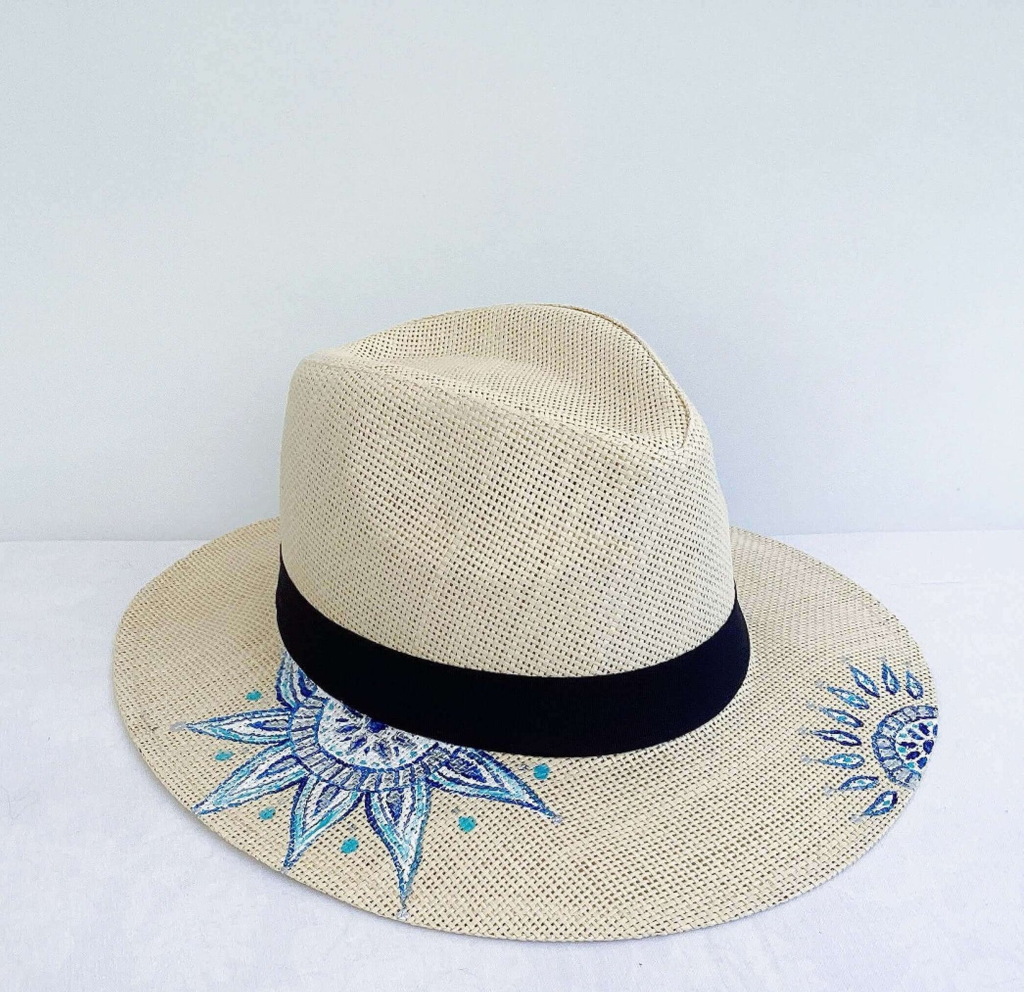 Side view of panama hat, black band at base, with hand painted blue mandalas asymmetrically positioned.