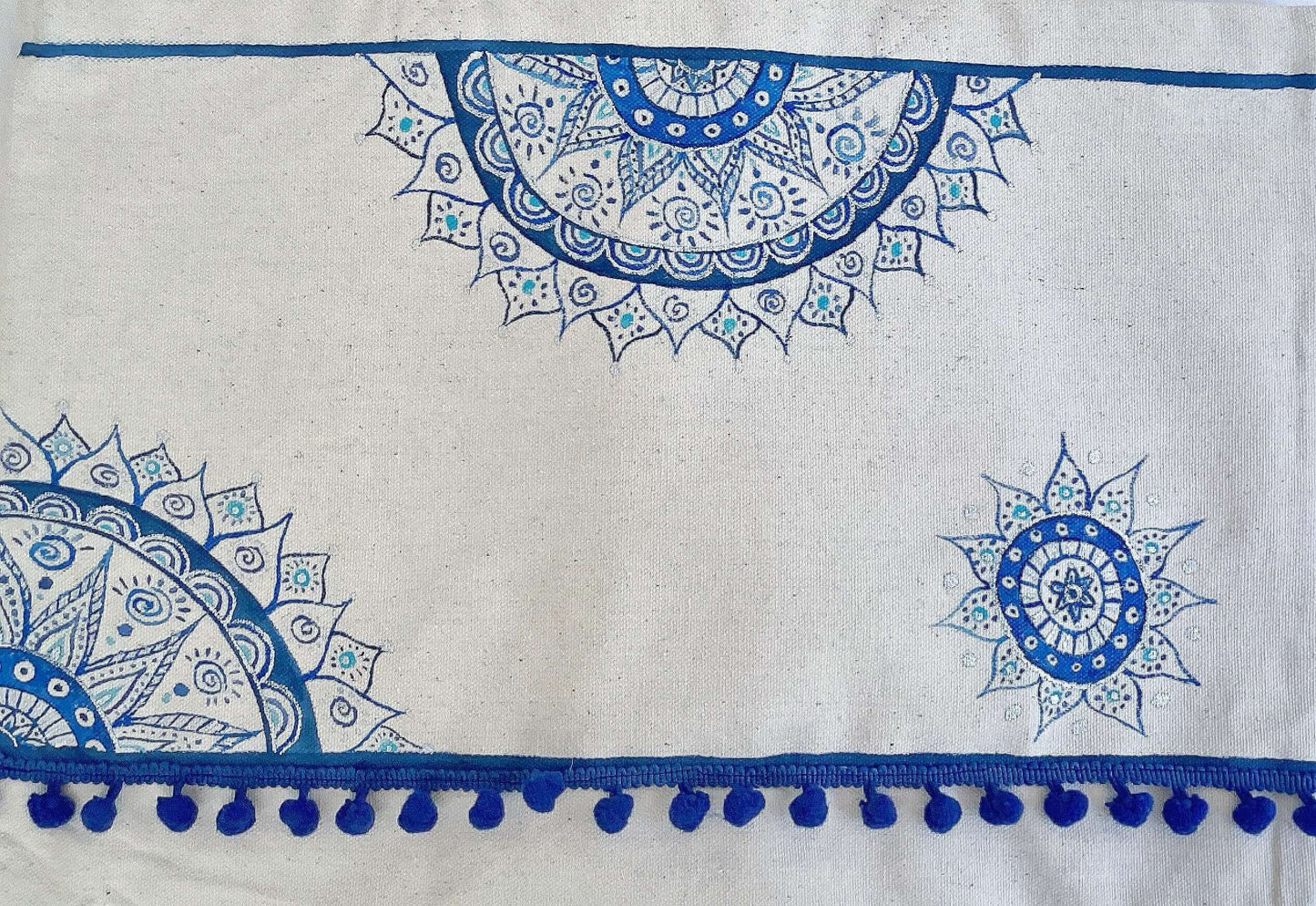 Detail view of tote bag with line of blue stitched pom poms, with blue painted mandalas here and there.