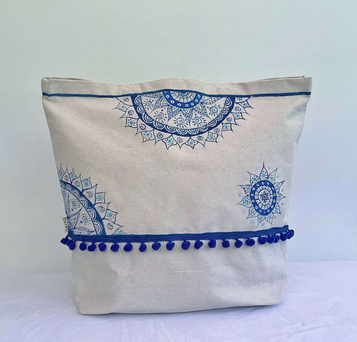 Front of tote bag with line of blue stitched pom poms, with blue painted mandalas here and there.