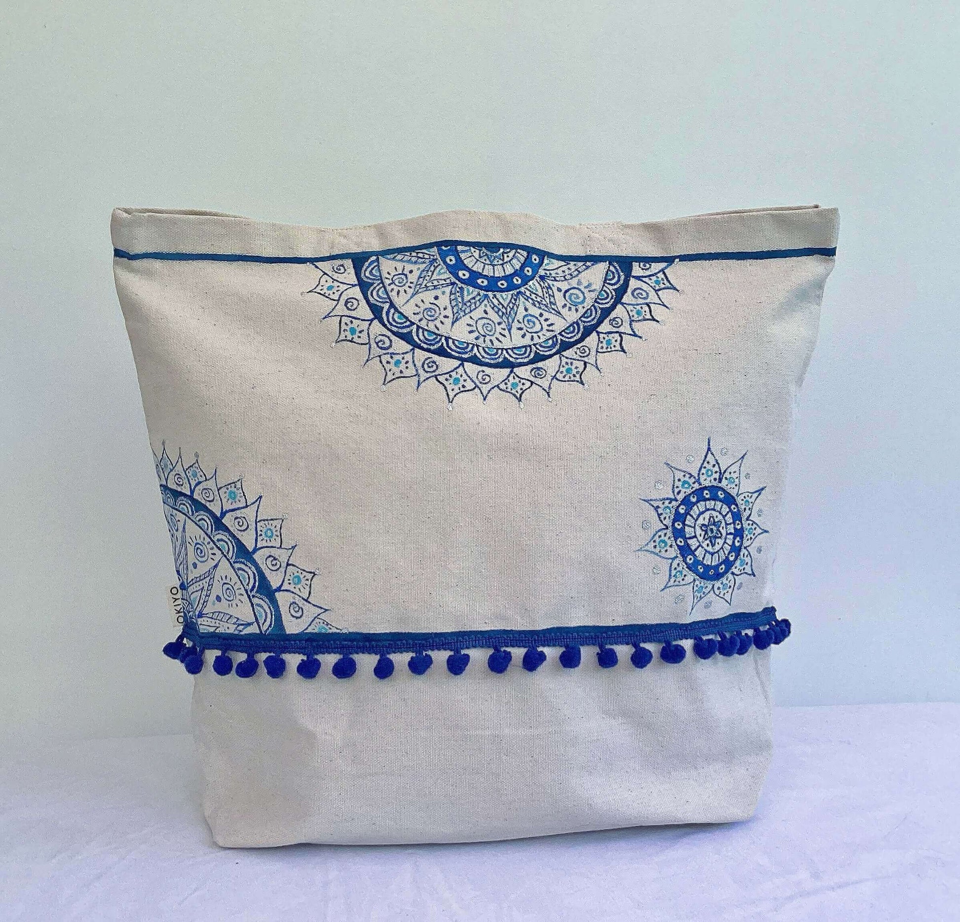 Front of tote bag with line of blue stitched pom poms, with blue painted mandalas here and there.