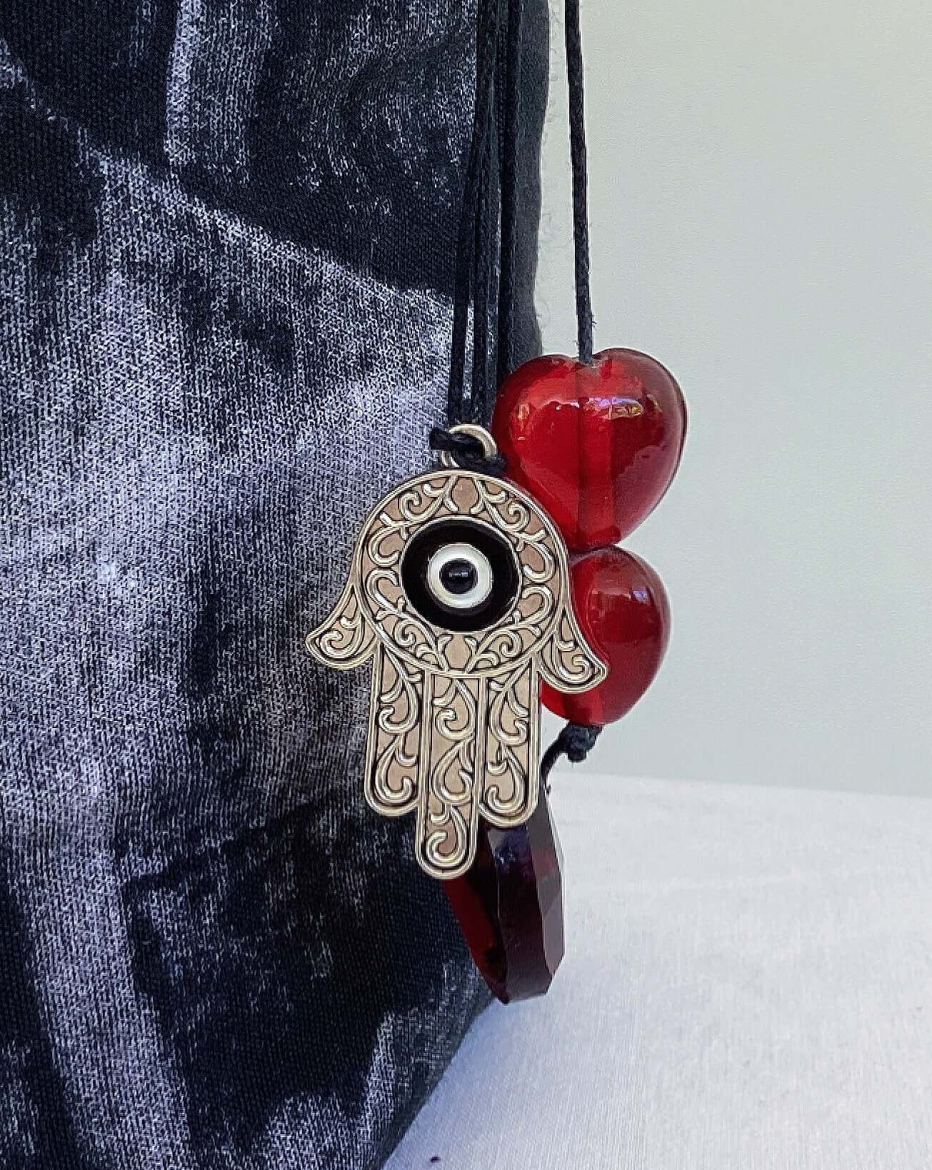 Close up of small metal hamsa charm and other beads dangling, attached to the strap.