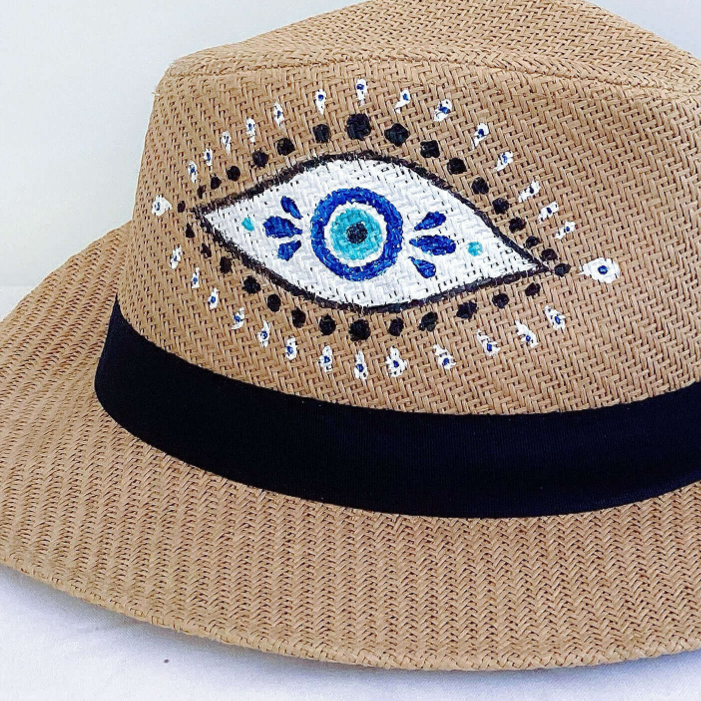 Close up view of panama hat, black band at base, hand painted blue, black and white evil eye.