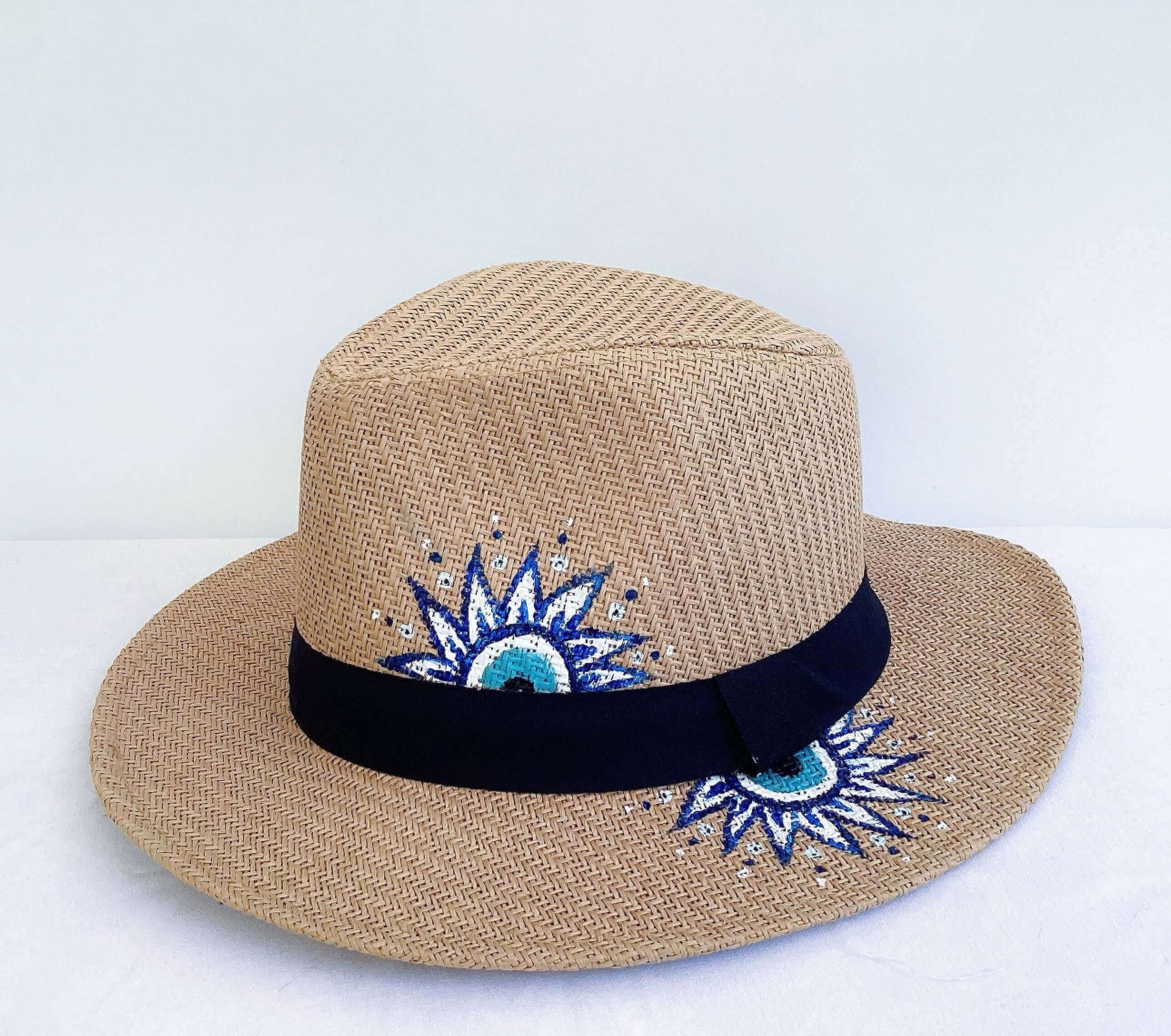 Side view of panama hat, black band at base, hand painted blue and white evil eye asymmetrically spaced.