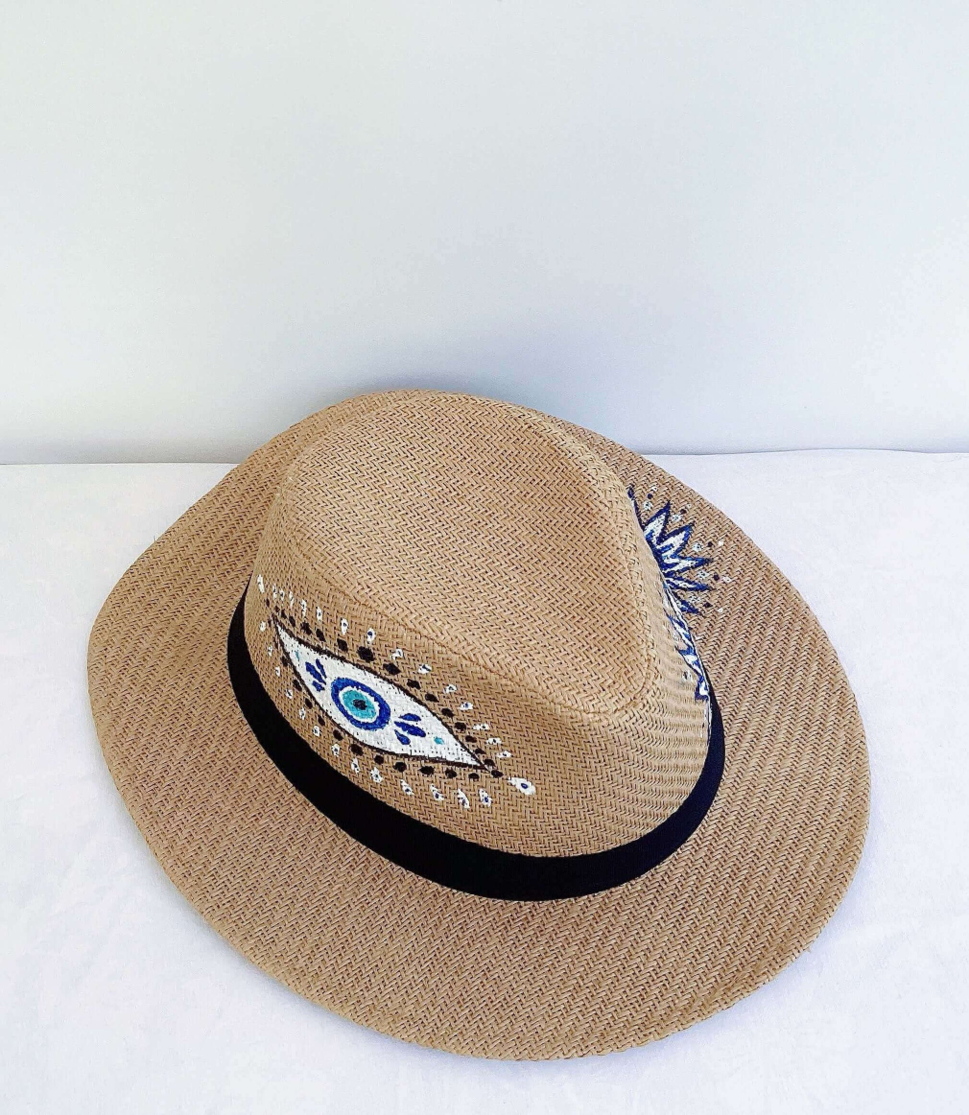 Front view of panama hat, black band at base, hand painted blue and white evil eye asymmetrically spaced.