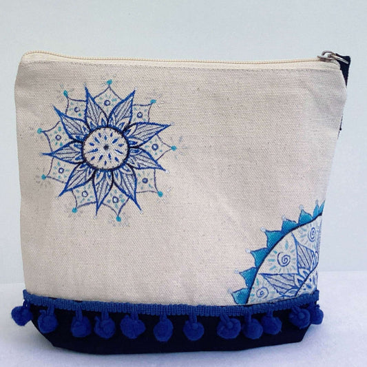 Front view of canvas make-up pouch, black canvas base, with hand painted blue mandalas and zip, blue pom pom fringe.