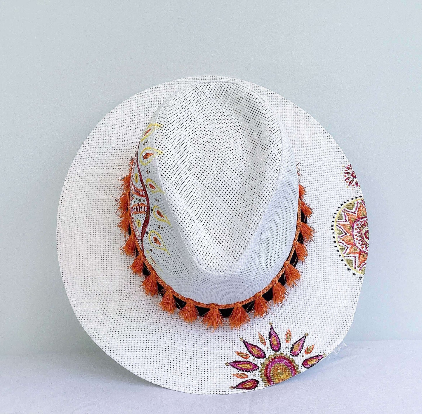 Aerial view of panama hat, black band at base, with hand painted red, gold and orange mandalas asymmetrically spaced.