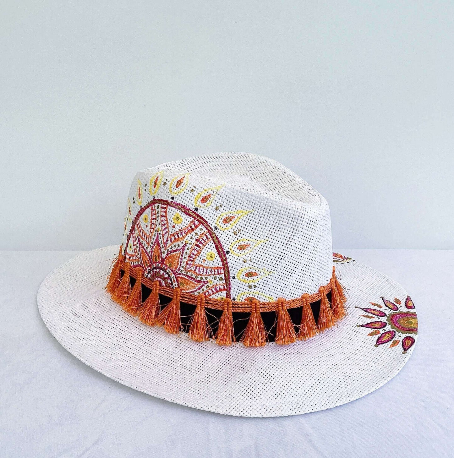 Detail of hat, black band with orange fringe at base, hand painted red, gold and orange mandalas asymmetrically spaced.