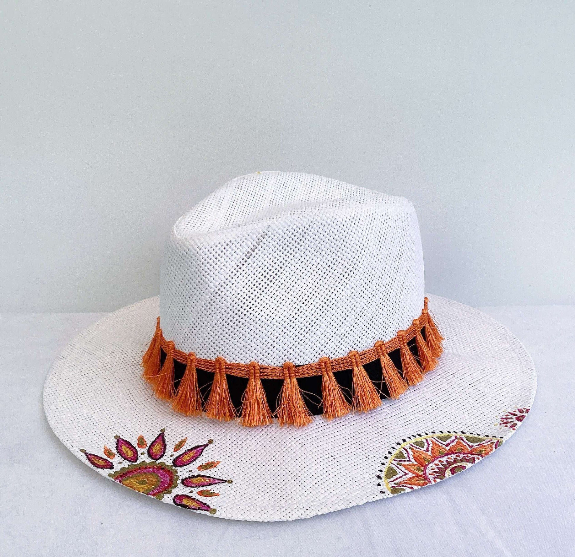 Top view of hat, black band at base with orange fringe, and hand painted red, gold, orange mandalas asymmetrically spaced.