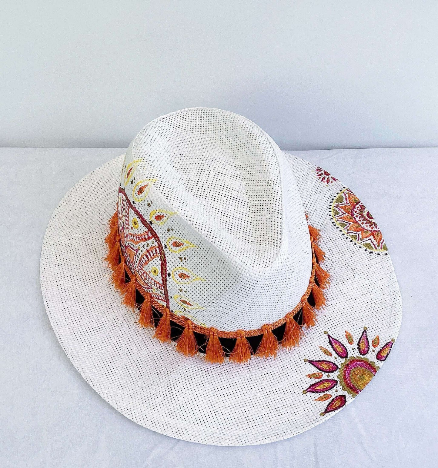 Side view of hat, black band with orange fringe, hand painted red, gold and orange mandalas asymmetrically spaced.