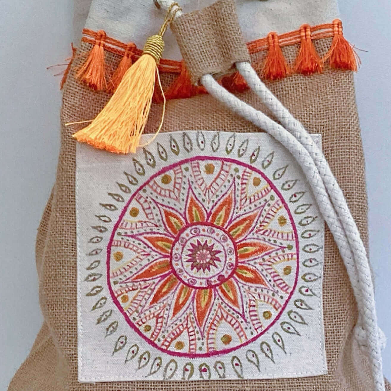 Detail view of hessian satchel with hand painted red, orange, gold mandala on canvas patch, with orange fringing at the top.