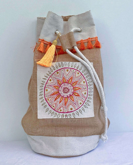 Front view of hessian satchel with hand painted red, orange, gold mandala on canvas patch, with orange fringing at the top.