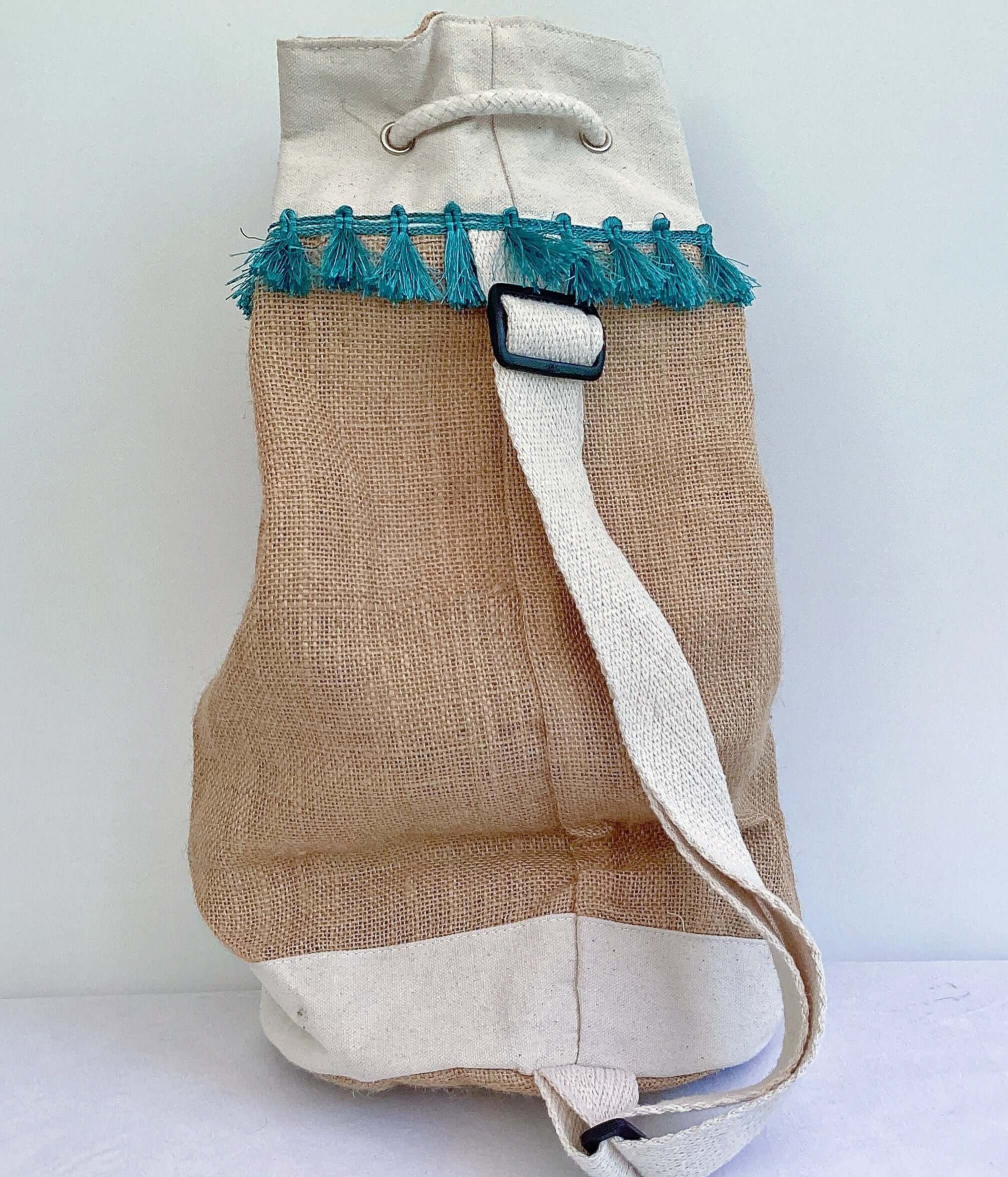 Back view of hessian satchel with teal fringing at the top, white back strap and base.