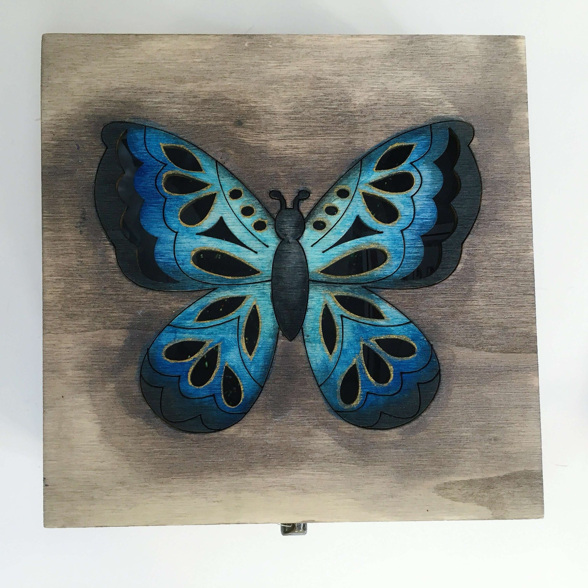 Detail view of painted lid, brown washed background, with multi blues butterfly in the center.