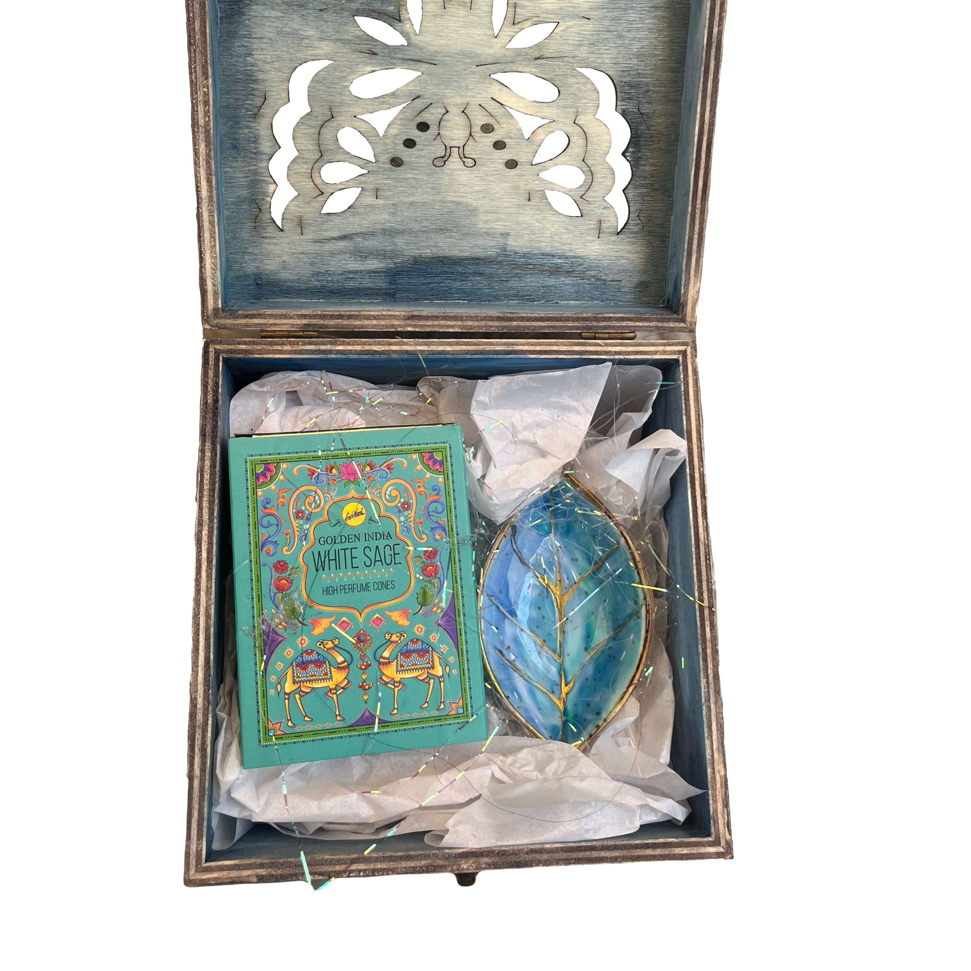 Contents view of incense and turquoise painted ceramic leaf, nestled in white tissue paper and tinsel.