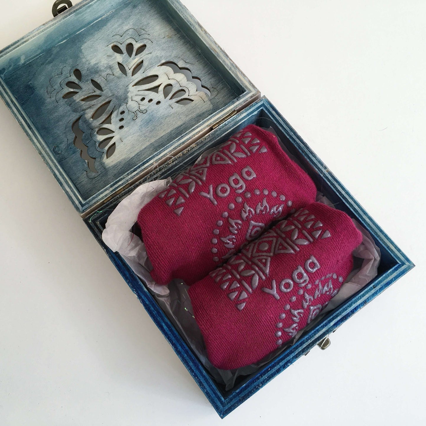 Contents view of plum yoga socks rolled up in box, nestled on white tissue paper in box.