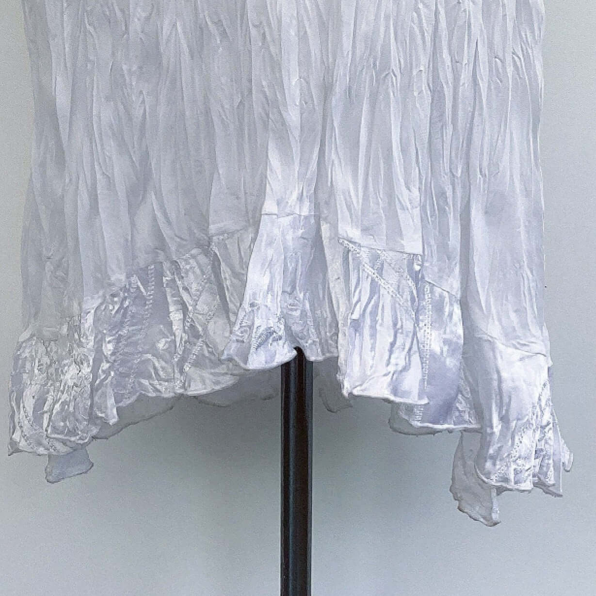 Close up of the embroidered white satin frill at the hem of the dress. 