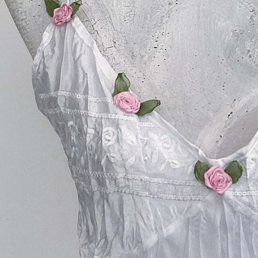 Detail view of white dress showing 5 pink roses with green leaves, stitched along the V neckline.