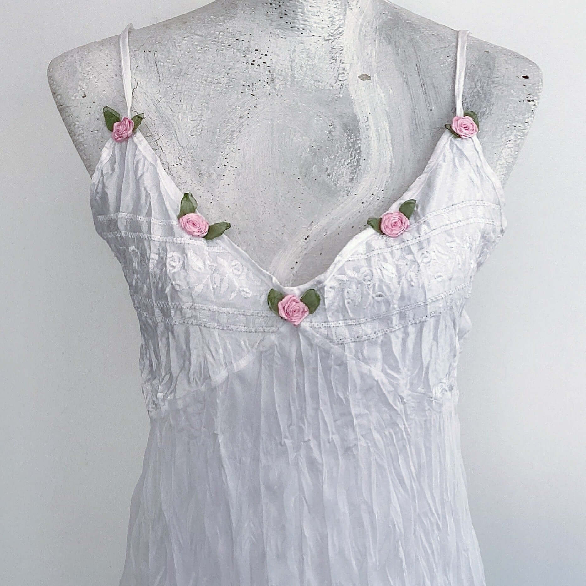 Close up of dress, with satin bust and straps, and 5 pink roses with green leaves, stitched along the V neckline.