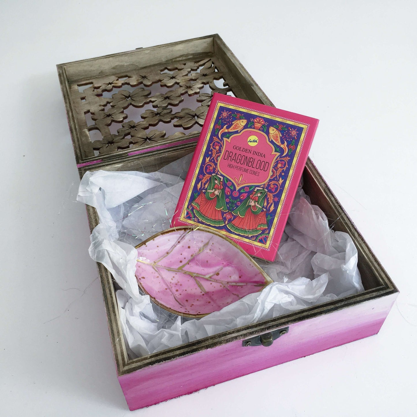 Contents view of incense and plum painted ceramic leaf, nestled in white tissue paper and tinsel.