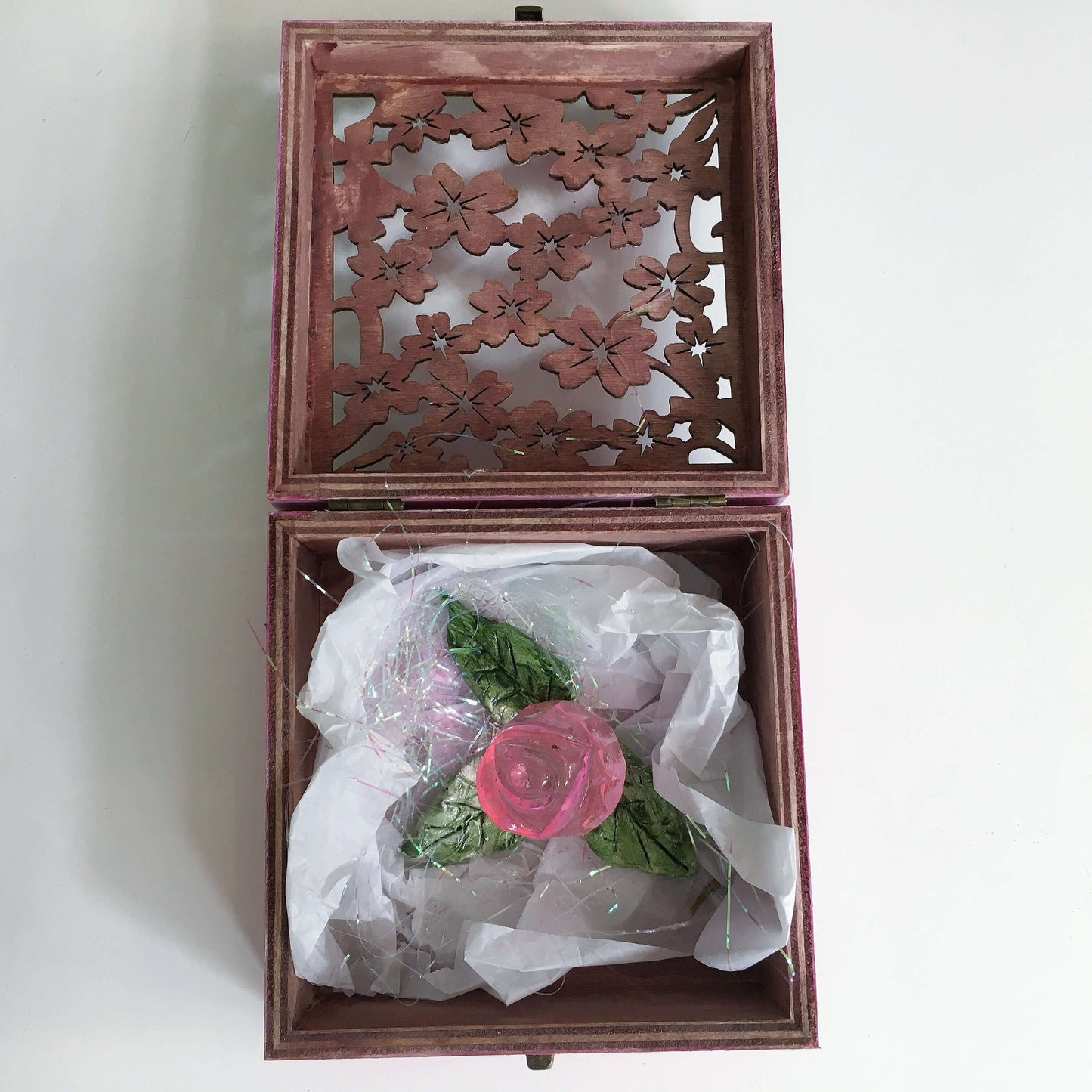 Contents of box, pink glass rosebud with handmade ceramic leaves nestled in tissue paper and tinsel.