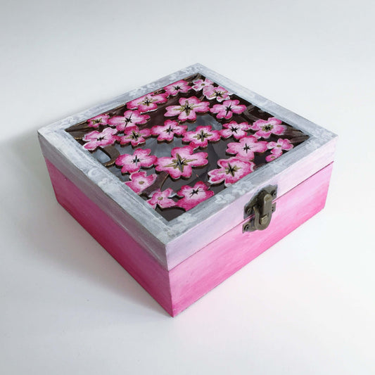 Outside view of pink painted box, fading to white and pink cherry blossom laser cut lid, with metal closing clasp.