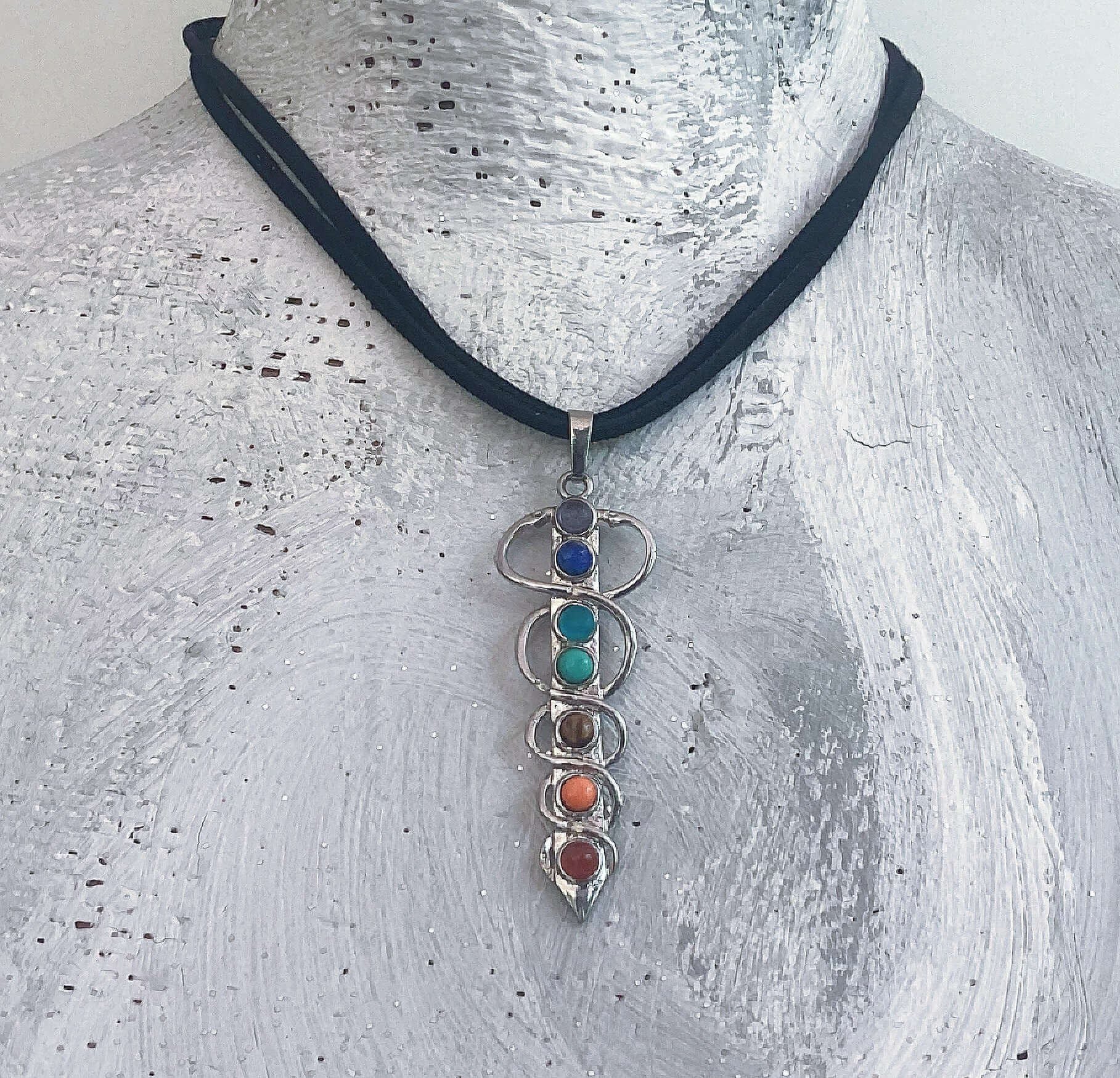 View of chakra colored stones in vertical carduceus design on choker, on white background.