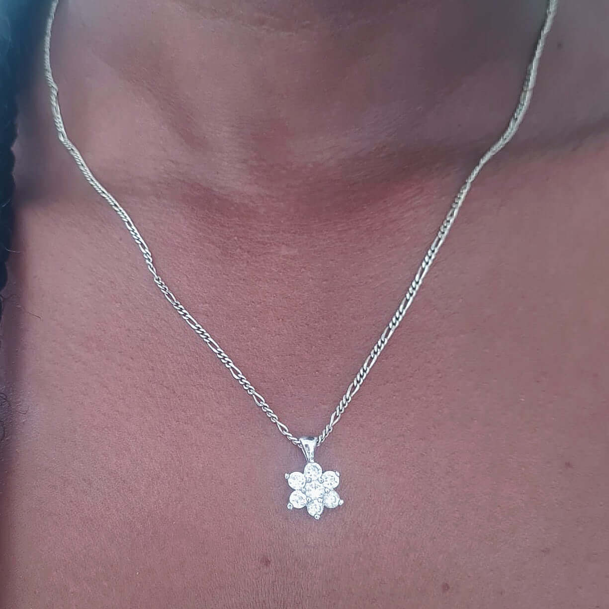 Flower shaped pendant with six cubic zirconia petals and a center on silver chain shown on neck.