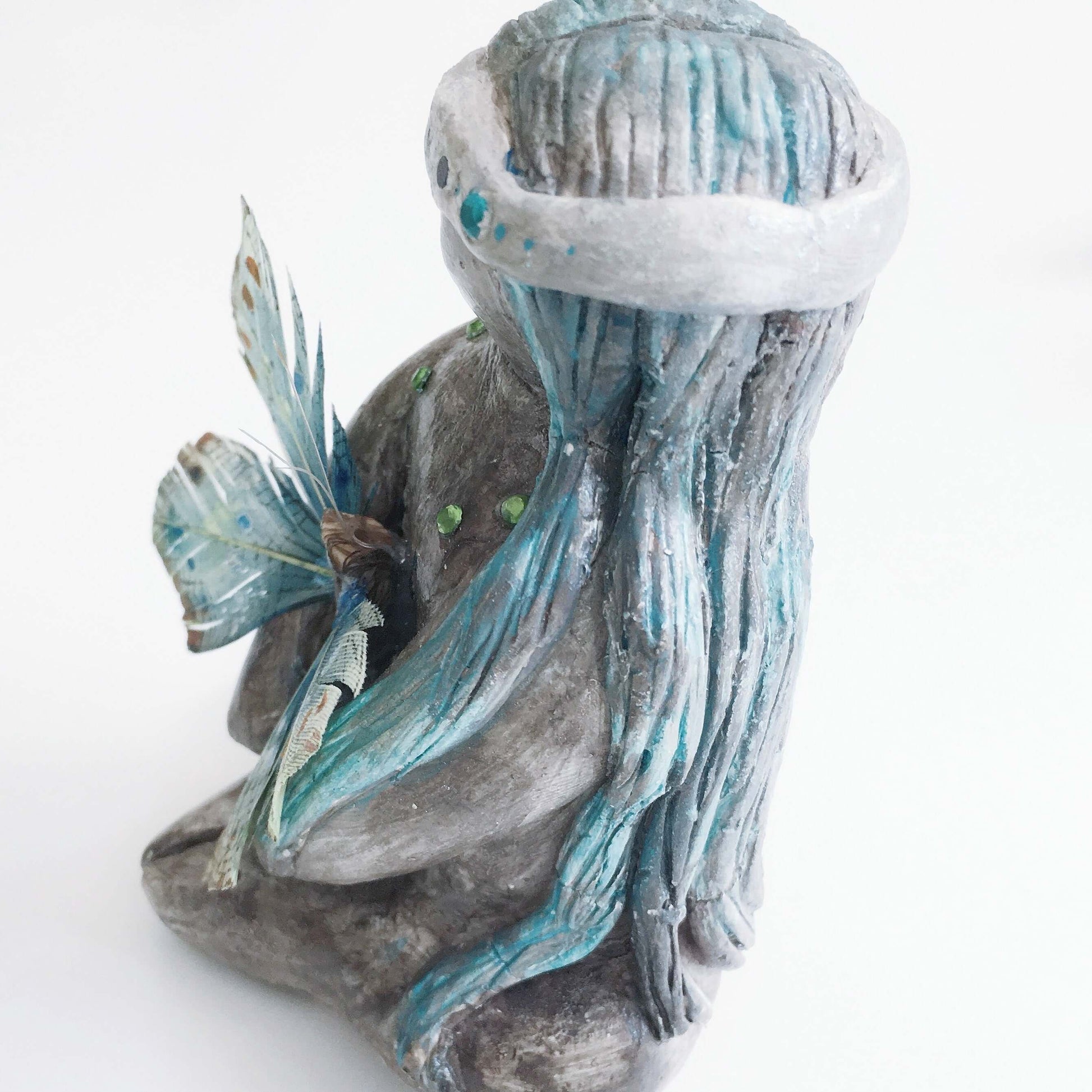 Side of elemental, brown wash painted figure, jewel band on head, bluish long hair, holding a feather butterfly.