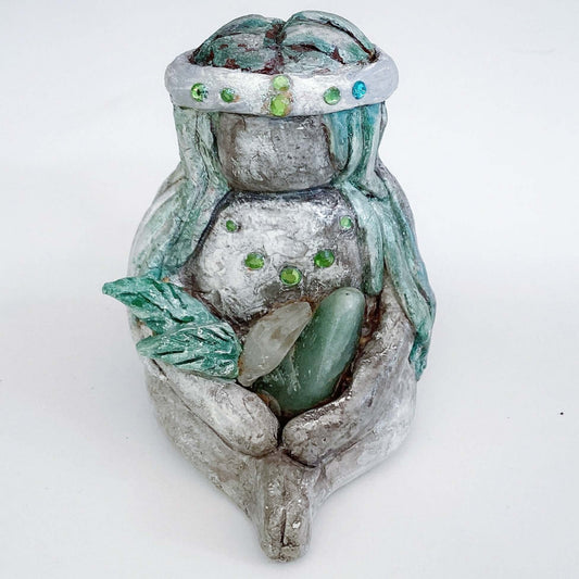 Front of elemental, brown wash painted figure, jewel band on head, pale green long hair, holding crystals and clay leaves.