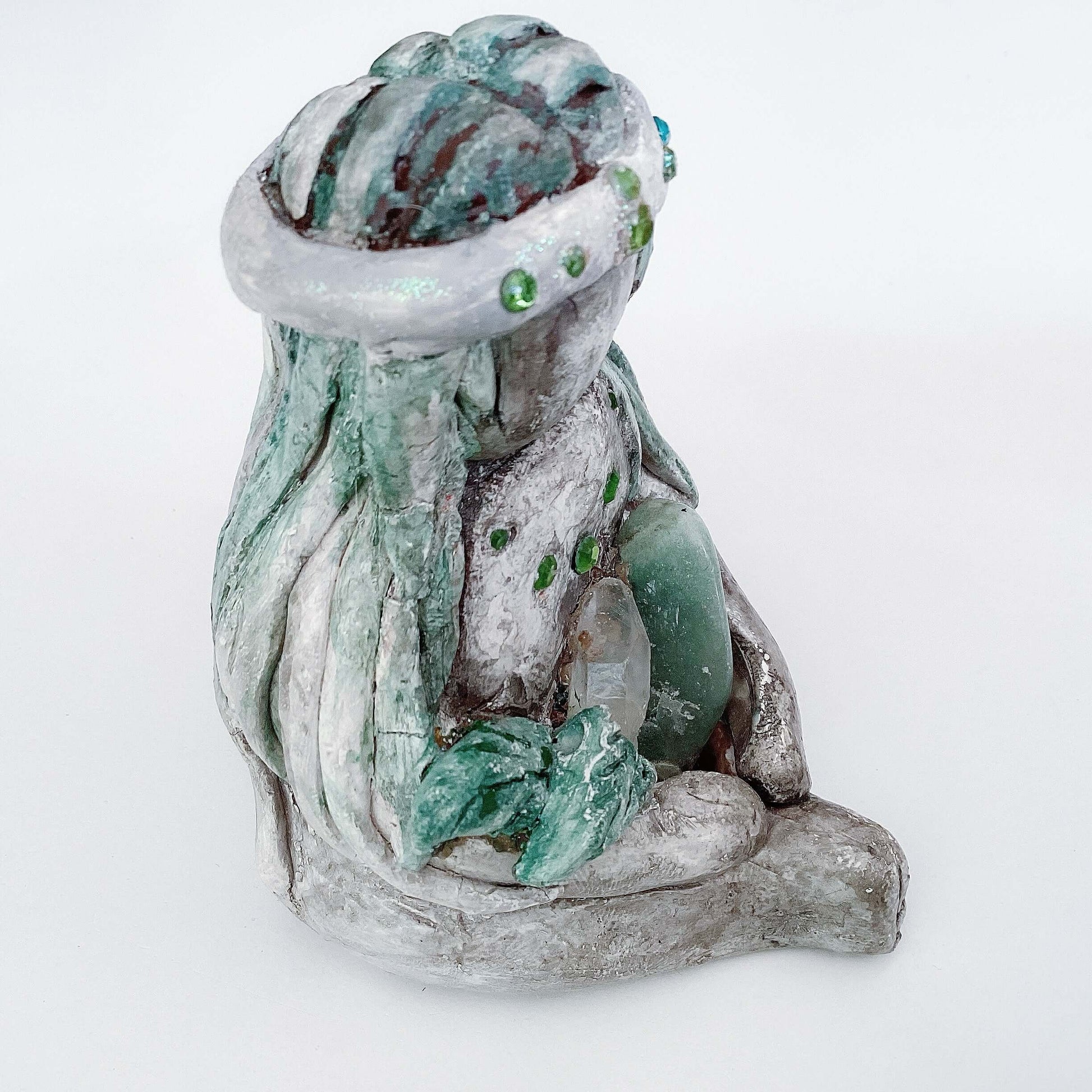 Side of elemental, brown wash painted figure, jewel band on head, pale green long hair, holding crystals and clay leaves.