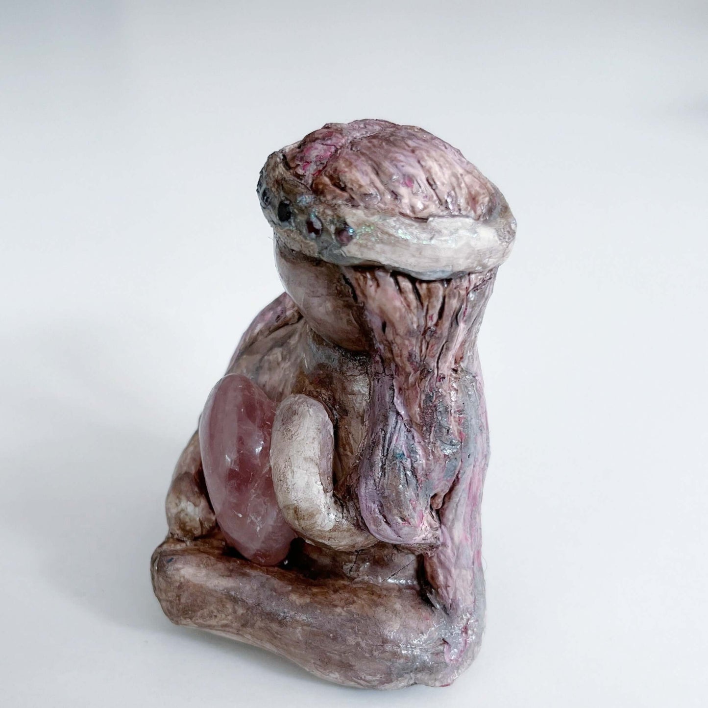 Left view of elemental, brown wash painted figure, jewel band on head, pink wash long hair, holding a tumbled rose quartz.
