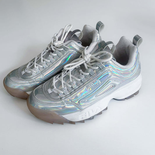 Side view of shoes, holographic material, with Fila name embedded in the sole of the shoes, white laces.