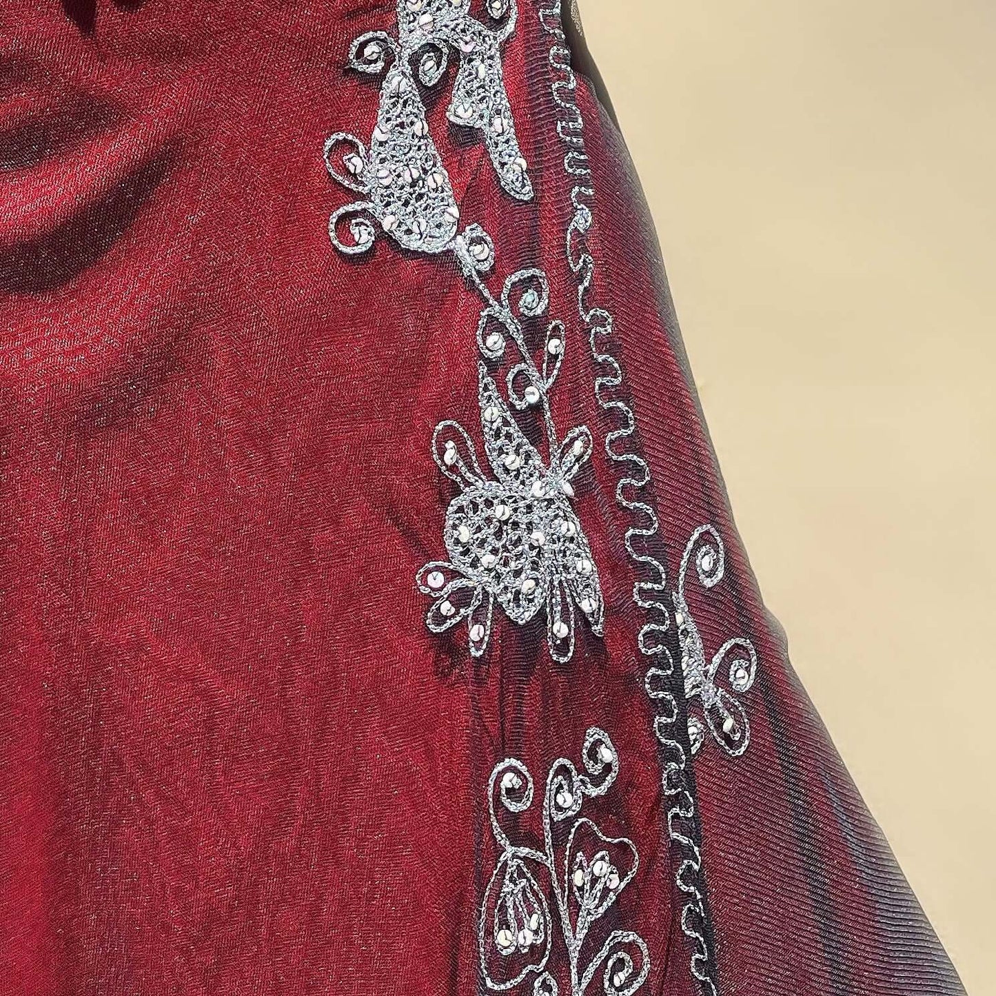 Detail view of the fabric, showing black net top layer with ornate silver embroidery and sequins, red viscose underlayer.