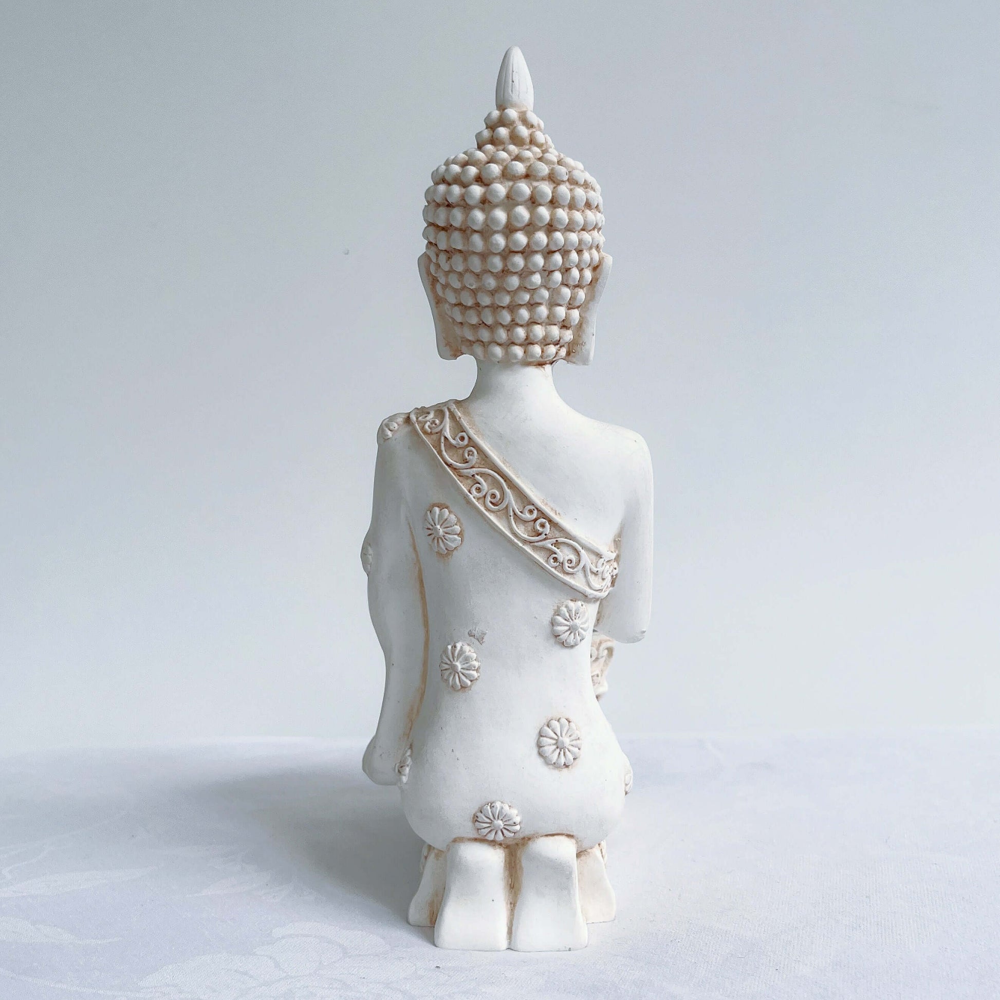 Back view of buddha kneeling, with ornate robes and detailing, natural off white colors.